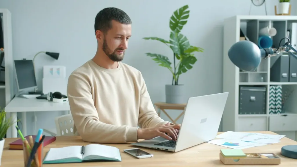 Person smiling while working on a laptop at a home desk