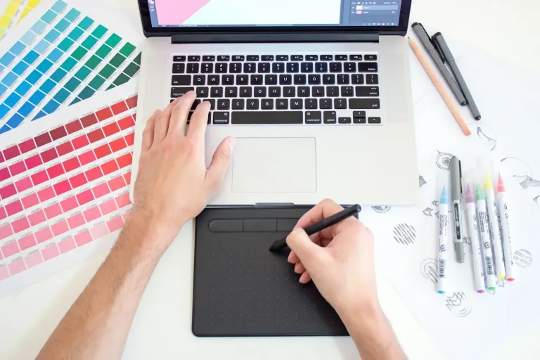 Designer working with a drawing tablet, laptop and colour swatches